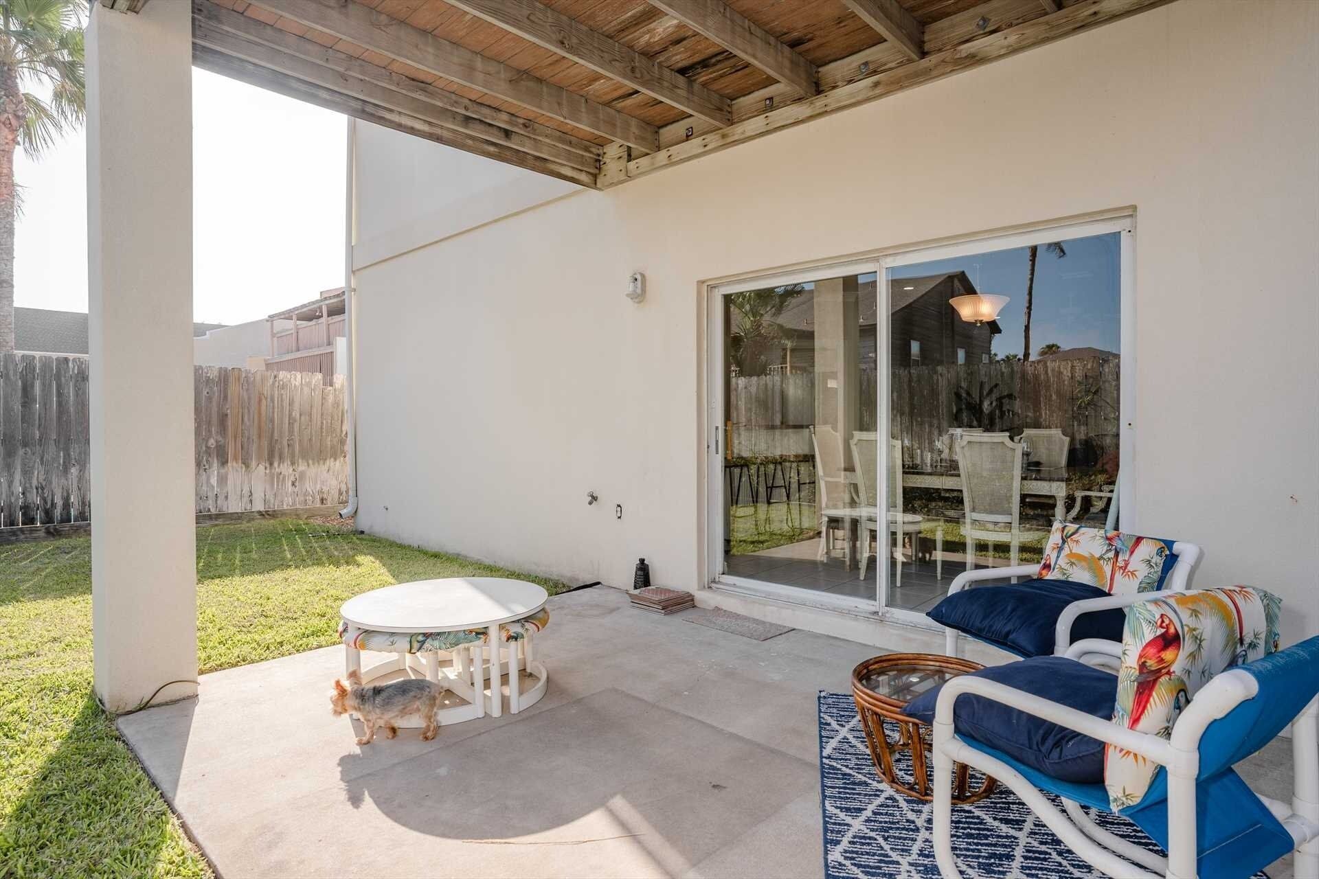 A covered patio with a round table, two wicker chairs, and a sliding glass door leading to an outdoor area.