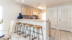 A kitchen with a central island, wooden cabinets, and a refrigerator. There are four stools around the island.