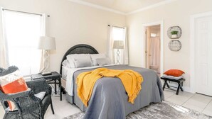 A bedroom with a bed, a chair, a bedside table, a lamp, and a door to the bathroom.
