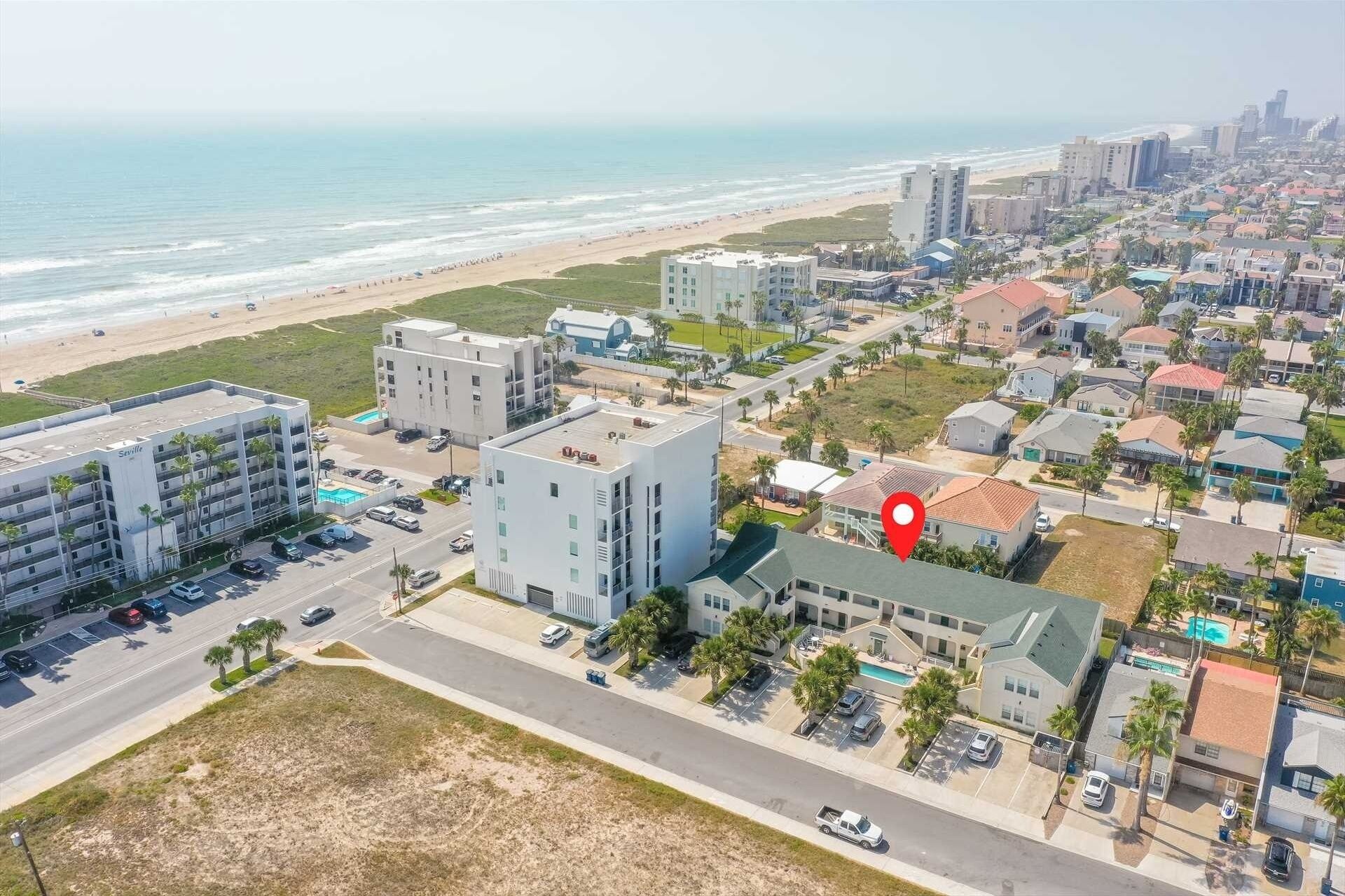Een kustplaats met een prominent hotel, compleet met een dakterraszwembad, omringd door woongebouwen en een strand.