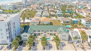 A coastal residential area with a large building featuring a green roof, multiple parking spaces, and a visible swimming pool.