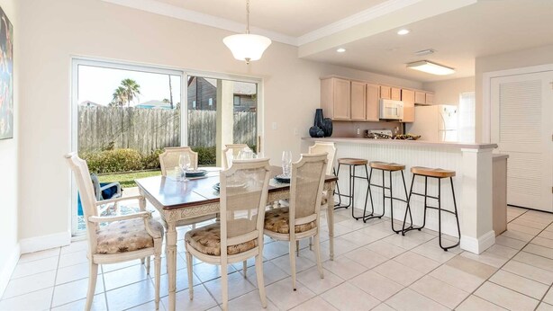 A dining area with a table and chairs, a kitchen with cabinets and appliances, and a view of the outdoors.