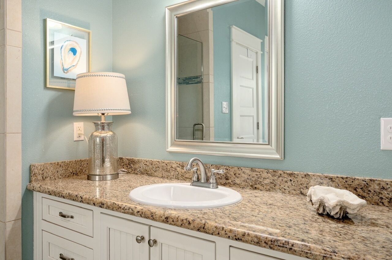 A bathroom with a granite countertop, a white sink, a silver faucet, a framed mirror, and a framed artwork on the wall.