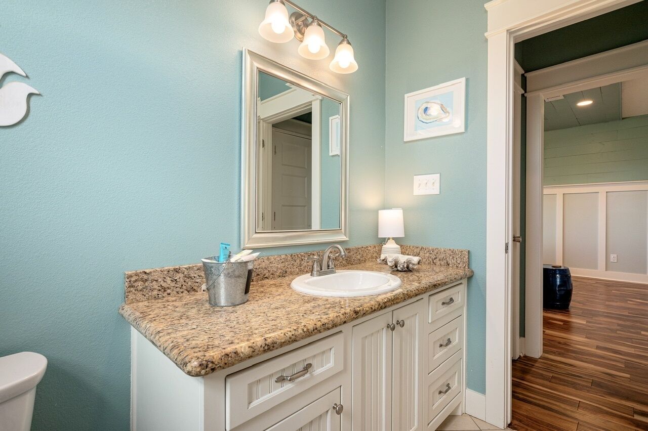 Un baño con encimera de granito, armarios blancos, un lavabo y un espejo con iluminación.
