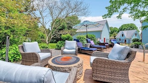 An outdoor patio with wicker furniture, a fire pit, and a blue house in the background. - Breathtaking Harwich Retreat w/ Heated Pool and Spa RPAM086 (Harwich)