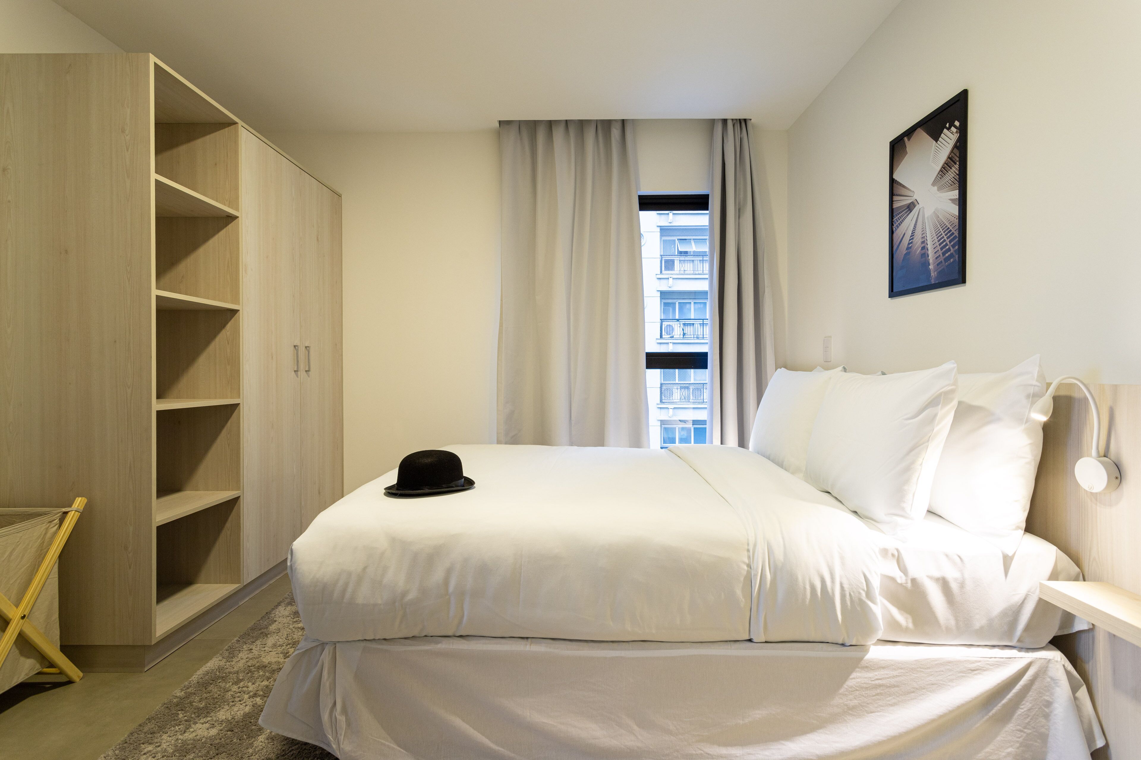 A hotel room with a large bed, a wardrobe, a window with curtains, and a wall-mounted light fixture.