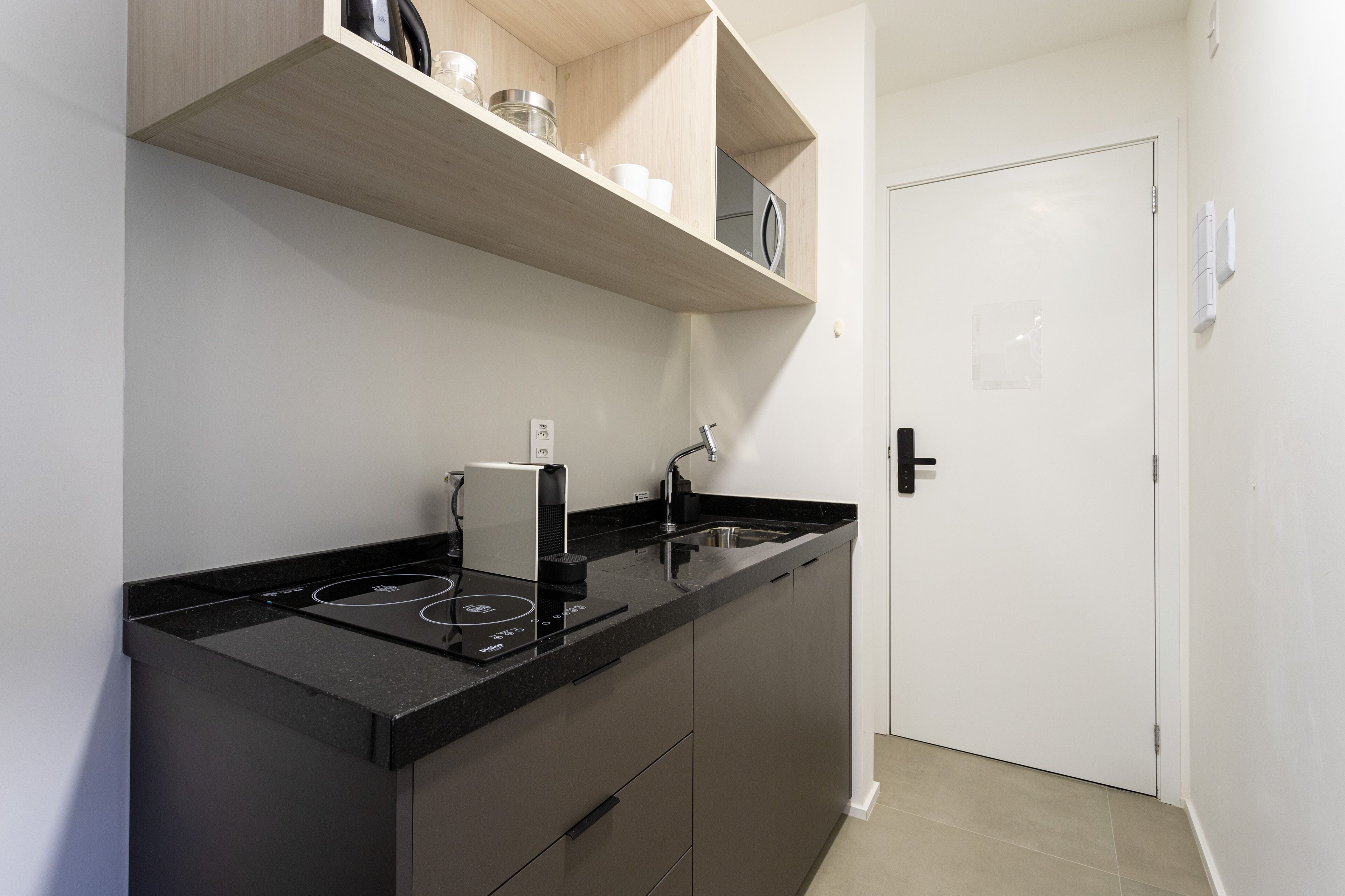 A modern kitchen with a black countertop, built-in oven, and a white door.