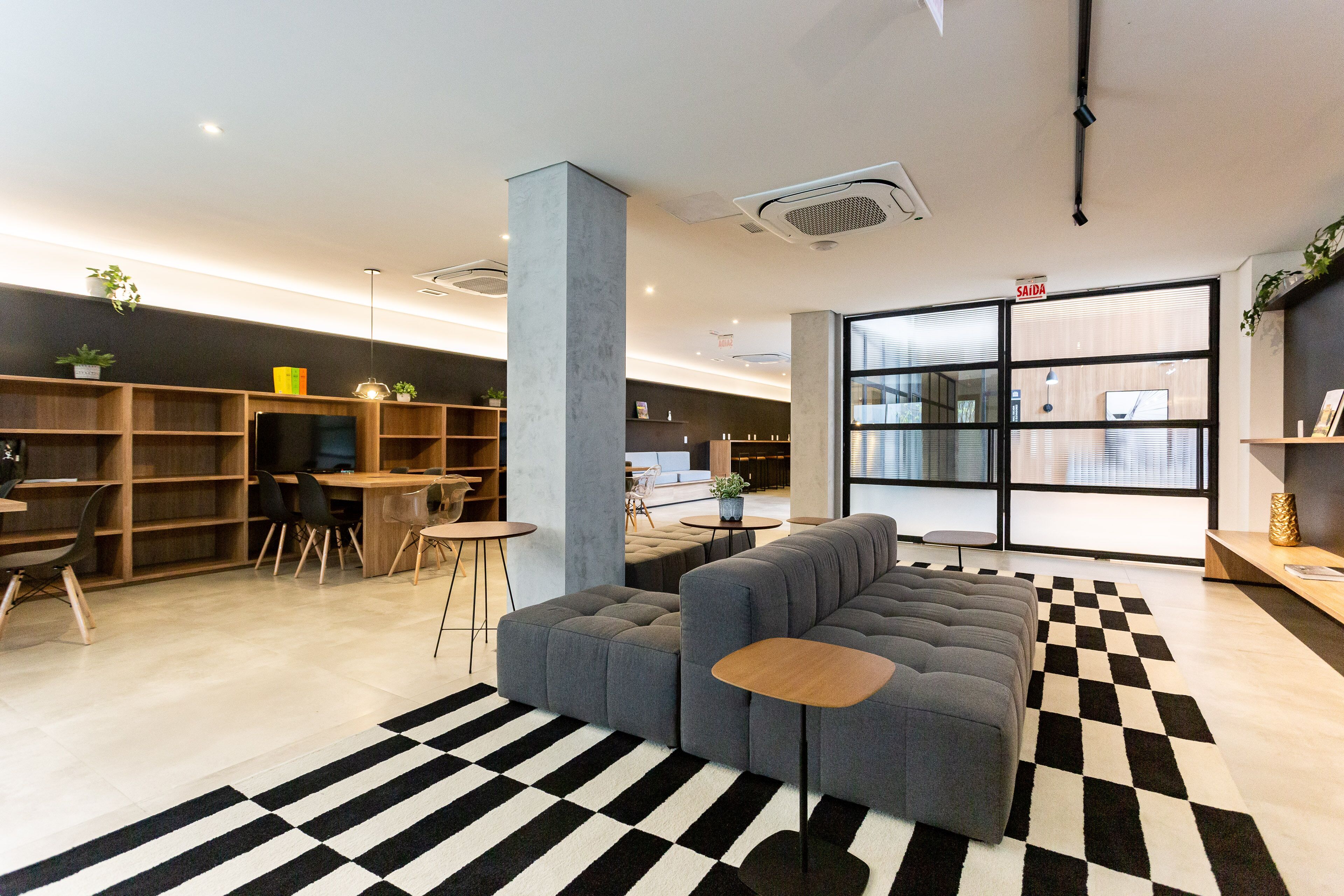 A modern lounge area with a checkered rug, a grey sectional sofa, and a small wooden table.