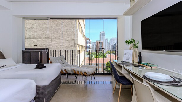 A modern hotel room with a balcony, a bed, a desk with a chair, and a television. - Charlie Sabiá Moema (São Paulo)