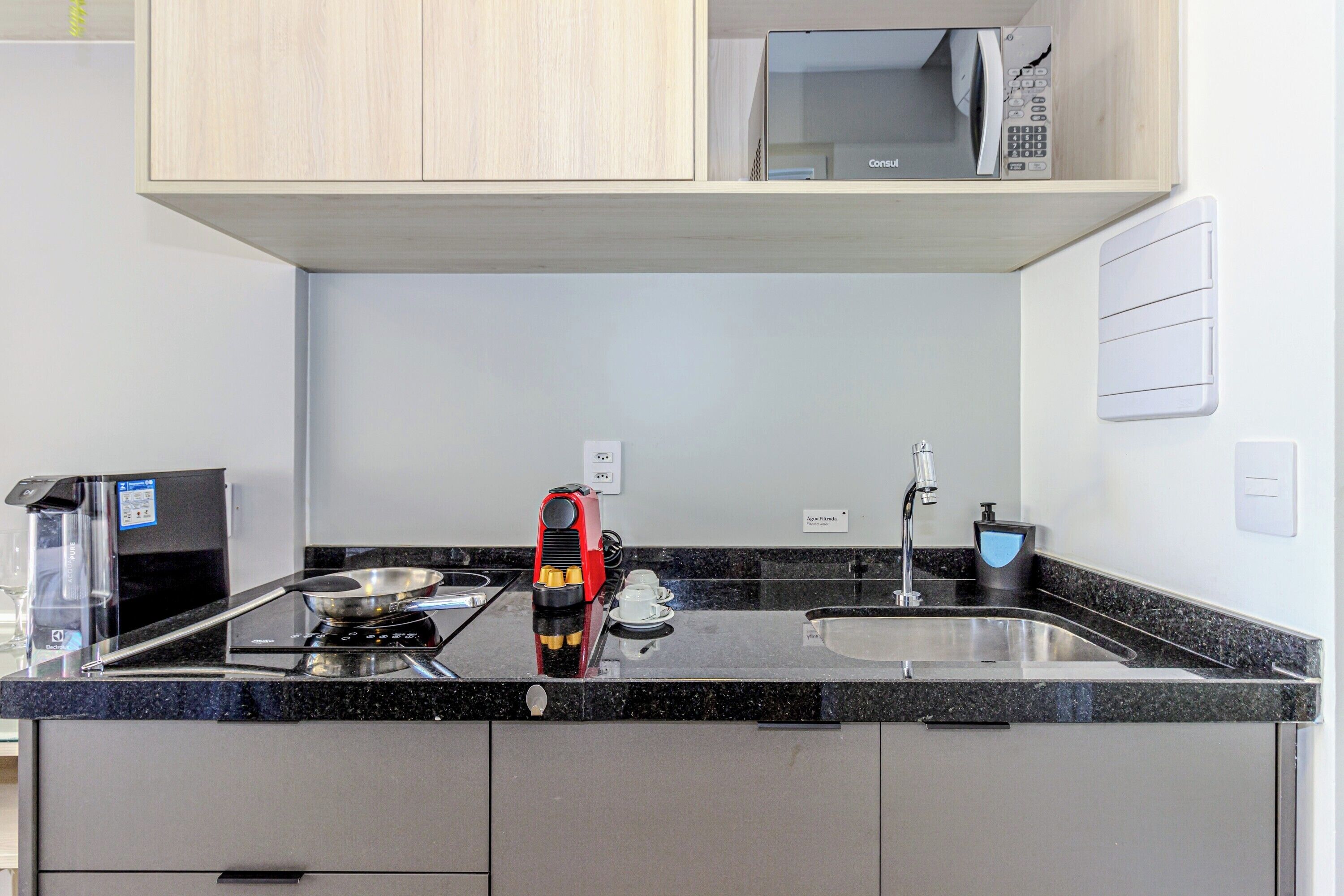 Una cocina compacta con microondas, cafetera y lavamanos.