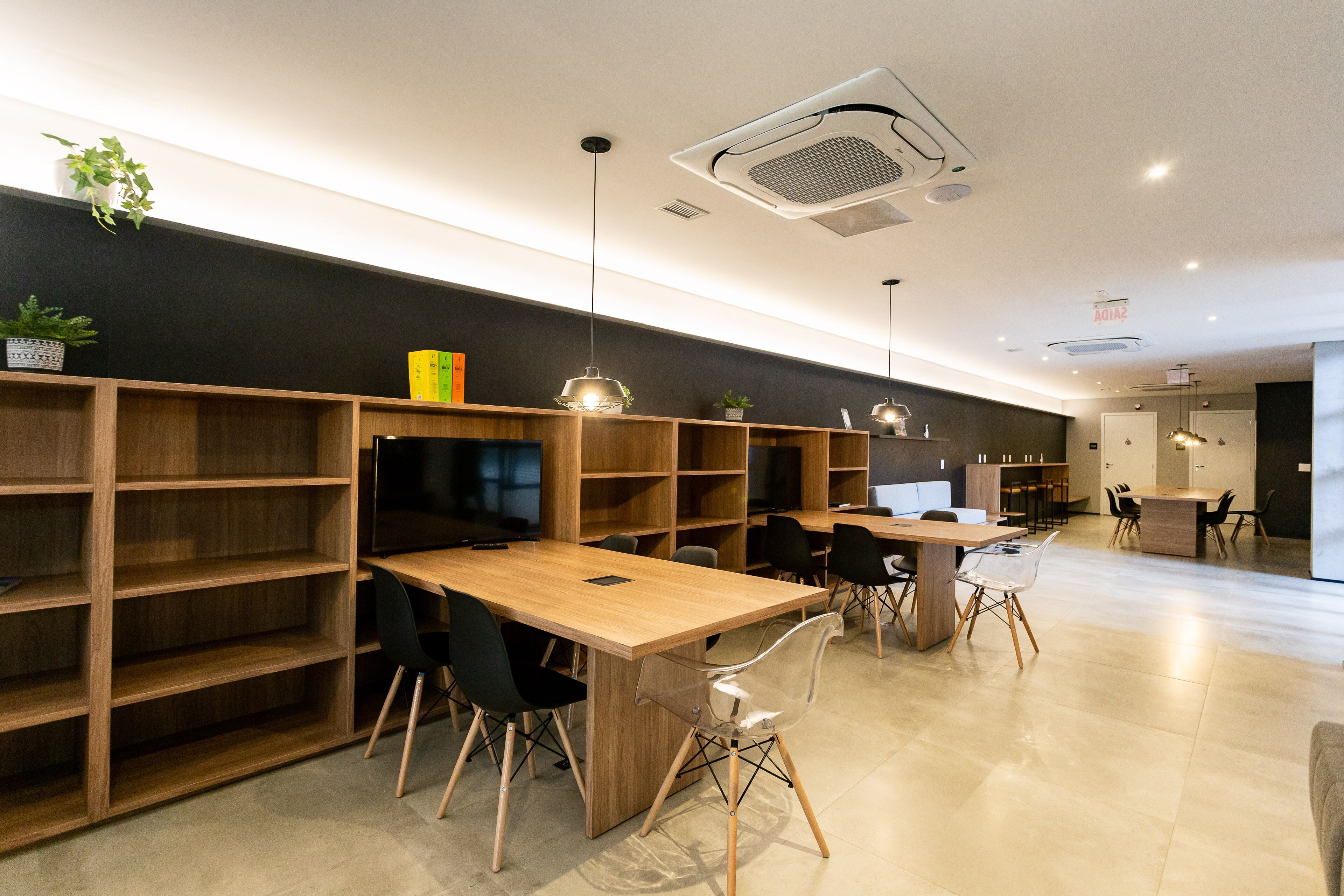 Une bibliothèque ou une salle de lecture moderne, avec des étagères en bois, des chaises noires et épurées, et une longue table en bois.