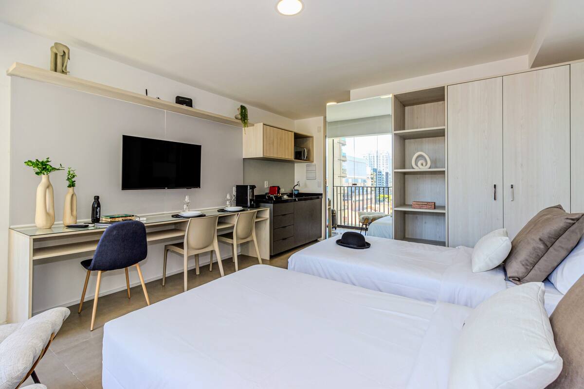 Ein modernes Hotelzimmer mit zwei Betten, einem Schreibtisch mit Stuhl, einem Fernseher und einem Balkon mit Blick auf die Stadt.