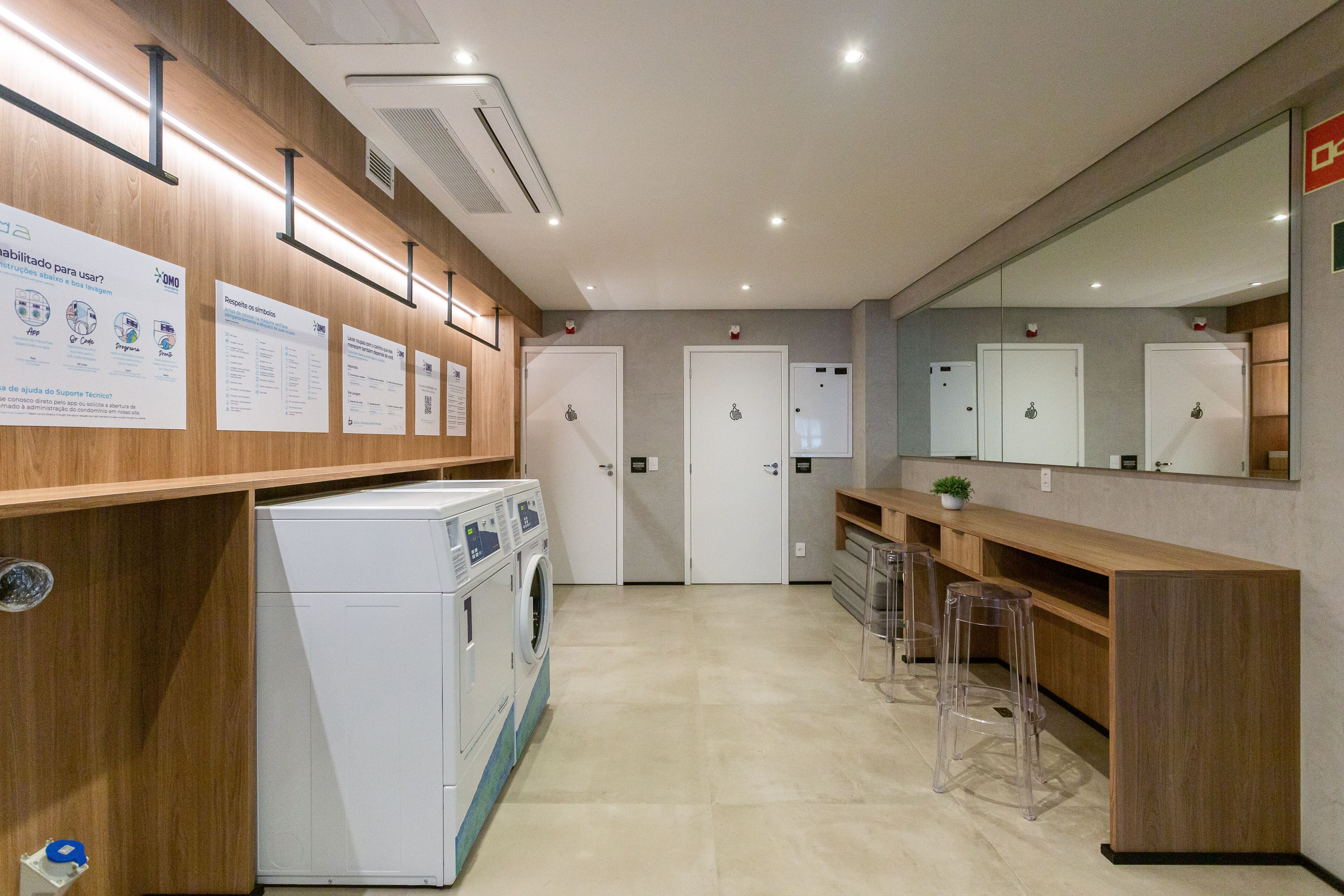 A modern laundry room with a washing machine, clear plastic stools, and a mirror.