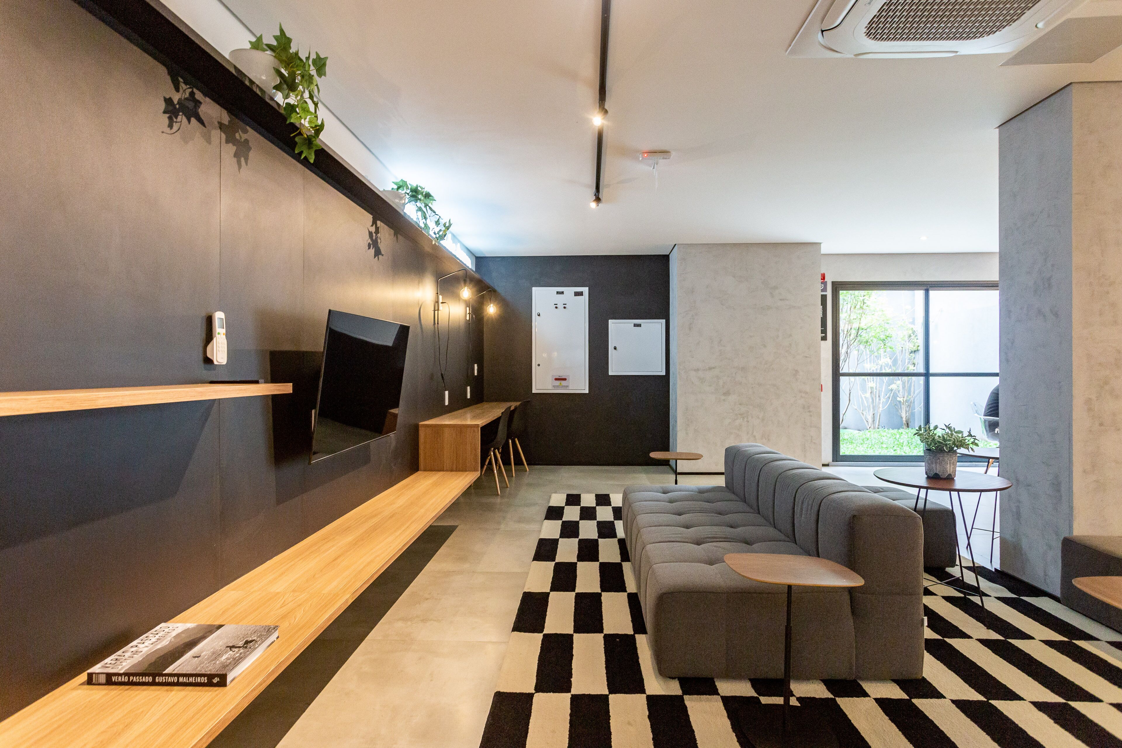 A modern lobby with a checkered floor, a grey sofa, a wooden reception desk, and a large TV screen.