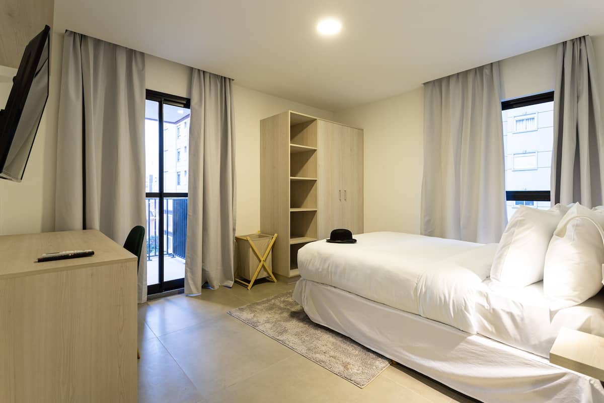 Ein Schlafzimmer mit Bett, Schreibtisch, Kleiderschrank und einem fensterbepflanzten Fenster.