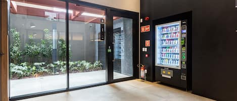 A modern lobby with a glass door leading to a courtyard, a vending machine, and a fire extinguisher.