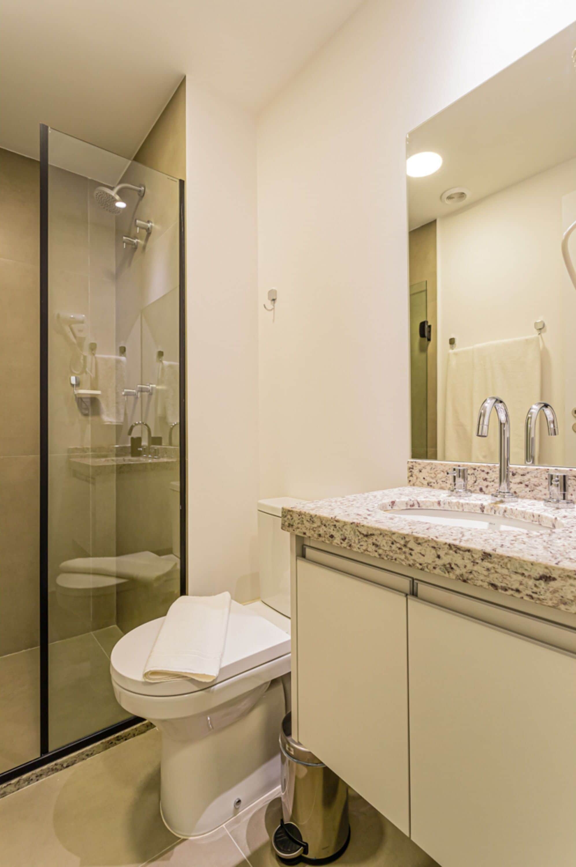 Un baño moderno con ducha de vidrio, inodoro blanco, lavamanos con encimera de mármol y un espejo grande.