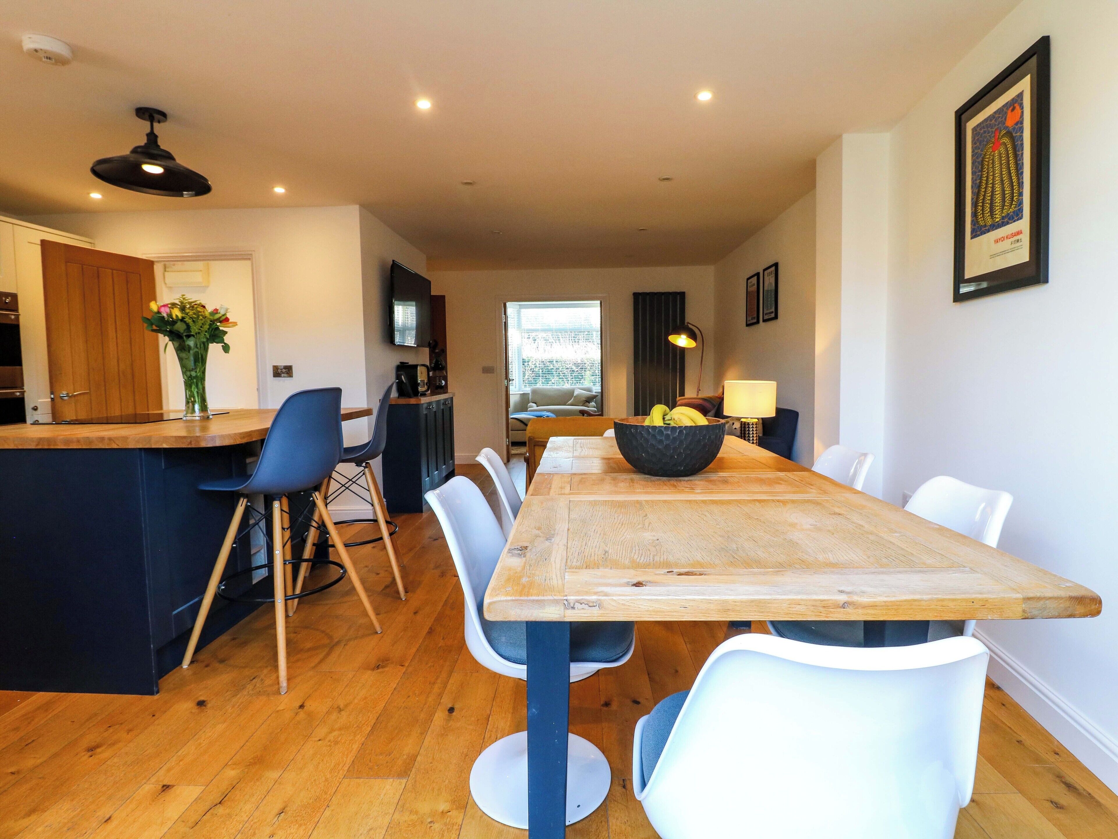 Una cocina moderna con una mesa de comedor de madera, sillas blancas y una isla central con un cuenco de fruta.