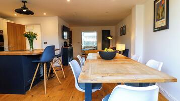 Una cocina moderna con una mesa de comedor de madera, sillas blancas y una isla central con un cuenco de fruta.