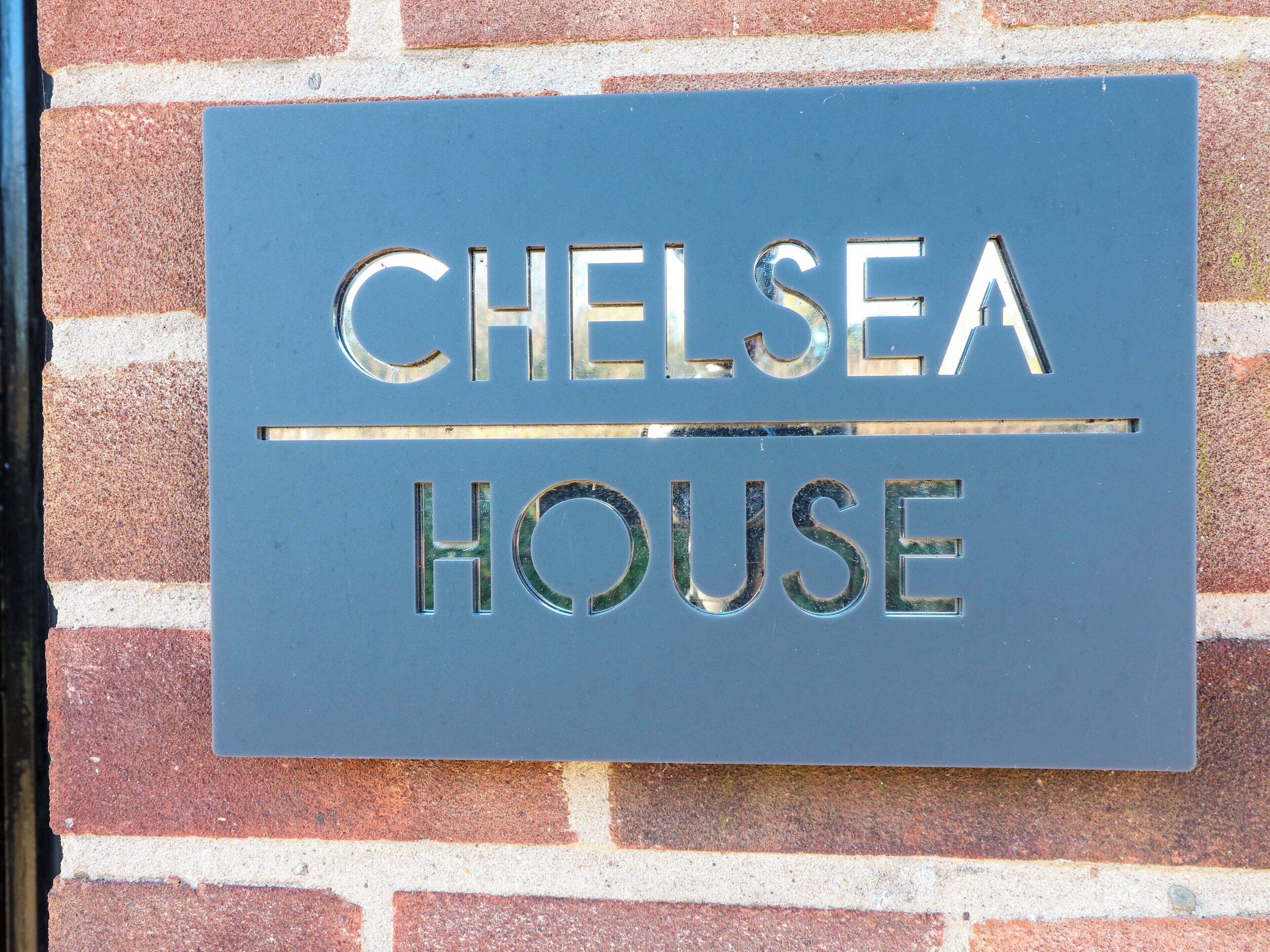 A sign with the words "CHELSEA HOUSE" on a brick wall.