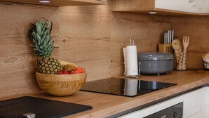 A modern kitchen with wooden cabinets, a wooden bowl of fruit, a black induction cooktop, and a grey slow cooker. - Villa Rosmarino Muntrilj with private pool (Muntrilj)