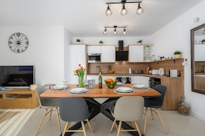 Una cocina moderna con armarios blancos, una mesa de comedor de madera y un televisor negro en la sala de estar.
