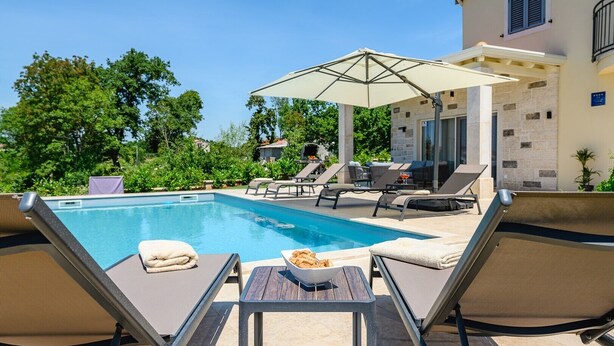 A poolside area with lounge chairs, a table with snacks, and a large umbrella. - Villa Rosmarino Muntrilj with private pool (Muntrilj)