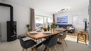 A modern living room with a dining area, featuring a large window, a black fireplace, and a cityscape painting on the wall. - Villa Rosmarino Muntrilj with private pool (Muntrilj)