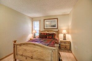 Un dormitorio con cama de madera, dos mesitas de noche, una ventana con persianas y un cuadro enmarcado en la pared.