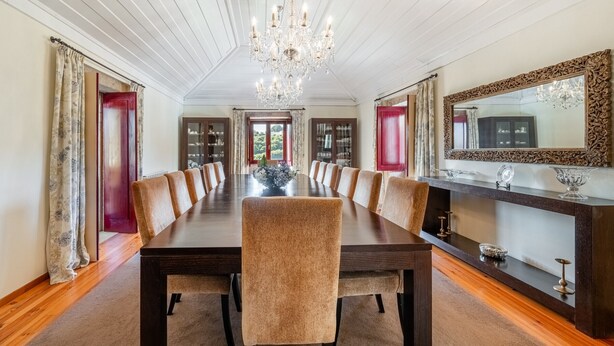 Een elegante eetzaal met een lange tafel, meerdere stoelen, een kroonluchter en een grote spiegel aan de muur.