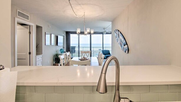 A modern kitchen with a large island, a dining area with a view, and a ceiling fan. - Fully Renovated Ocean Front Condo at Sea Colony (Sussex County)
