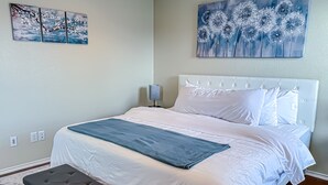 Ein Schlafzimmer mit einem großen Bett, weißer Bettwäsche, einer grauen Bank und zwei Wandbildern.