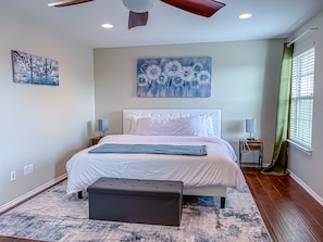A bedroom with a bed, bedside tables, a ceiling fan, artwork on the walls, and a window with blinds. - Spacious 5-King Bed Mansion | 15 Min to Downtown Austin (Pflugerville)