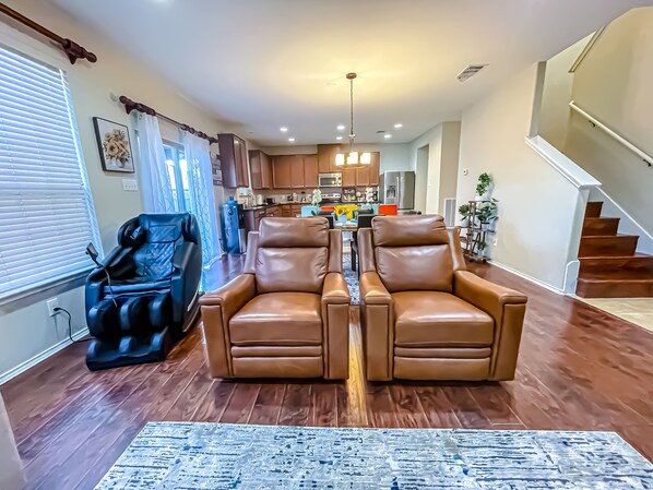 A spacious living room with a brown leather sofa set, a blue massage chair, and a patterned rug.