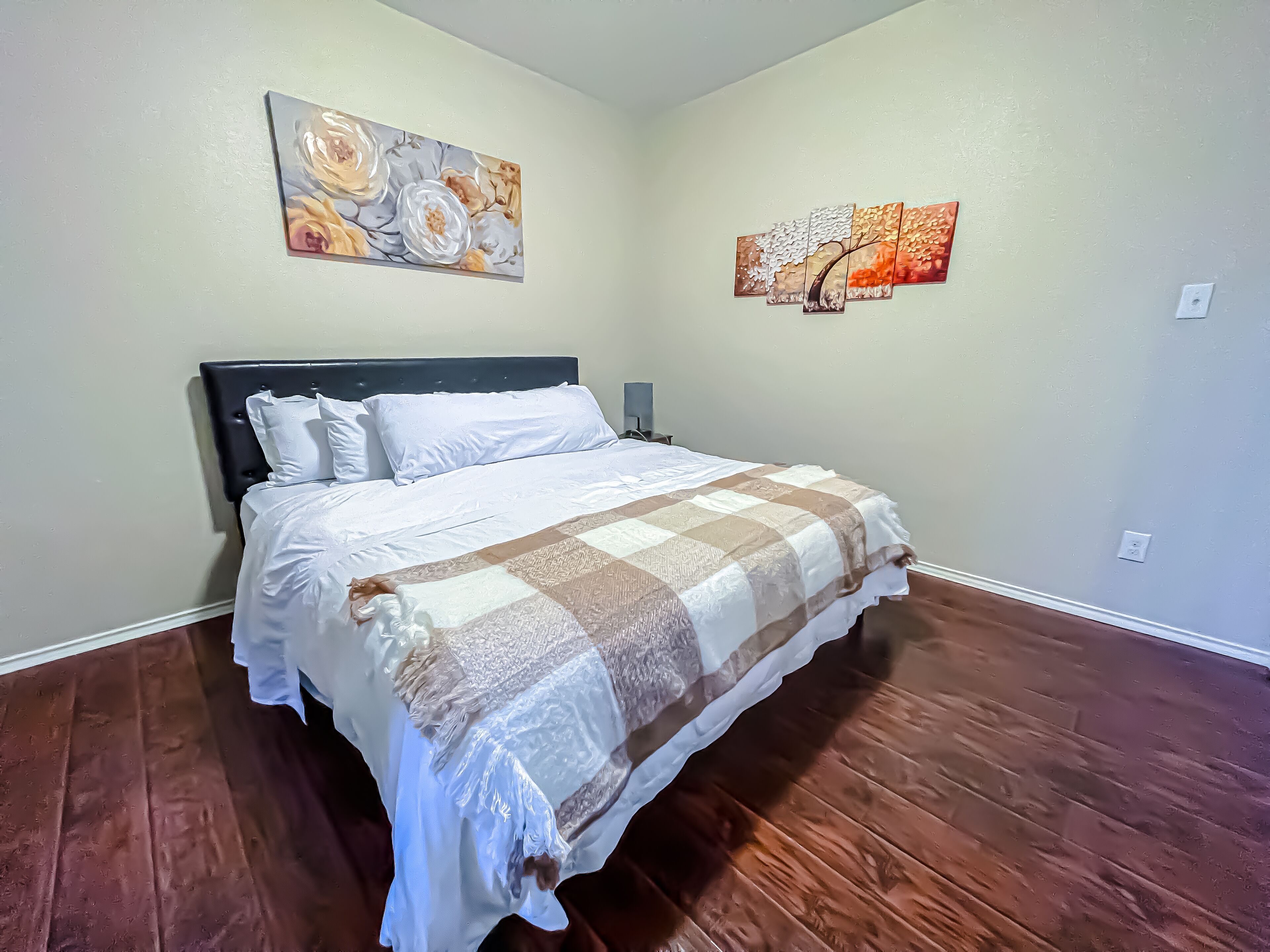 Une chambre avec un grand lit, deux tableaux accrochés au mur et un plancher en bois massif.
