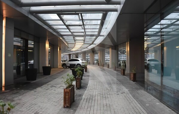 Un edificio moderno con fachada de vidrio, una galería techada y plantas en macetas a lo largo del camino.