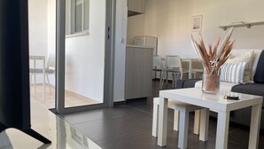 A modern living room with a white sofa, a glass coffee table, and a dining area with a white table and chairs. - Phaedrus Living City Flat Demetra 102 (Larnaca)