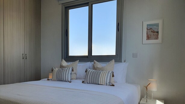 A bedroom with a large bed, two bedside tables, a wardrobe, and a window with a view of the beach. - Phaedrus Living City Flat Demetra 102 (Larnaca)
