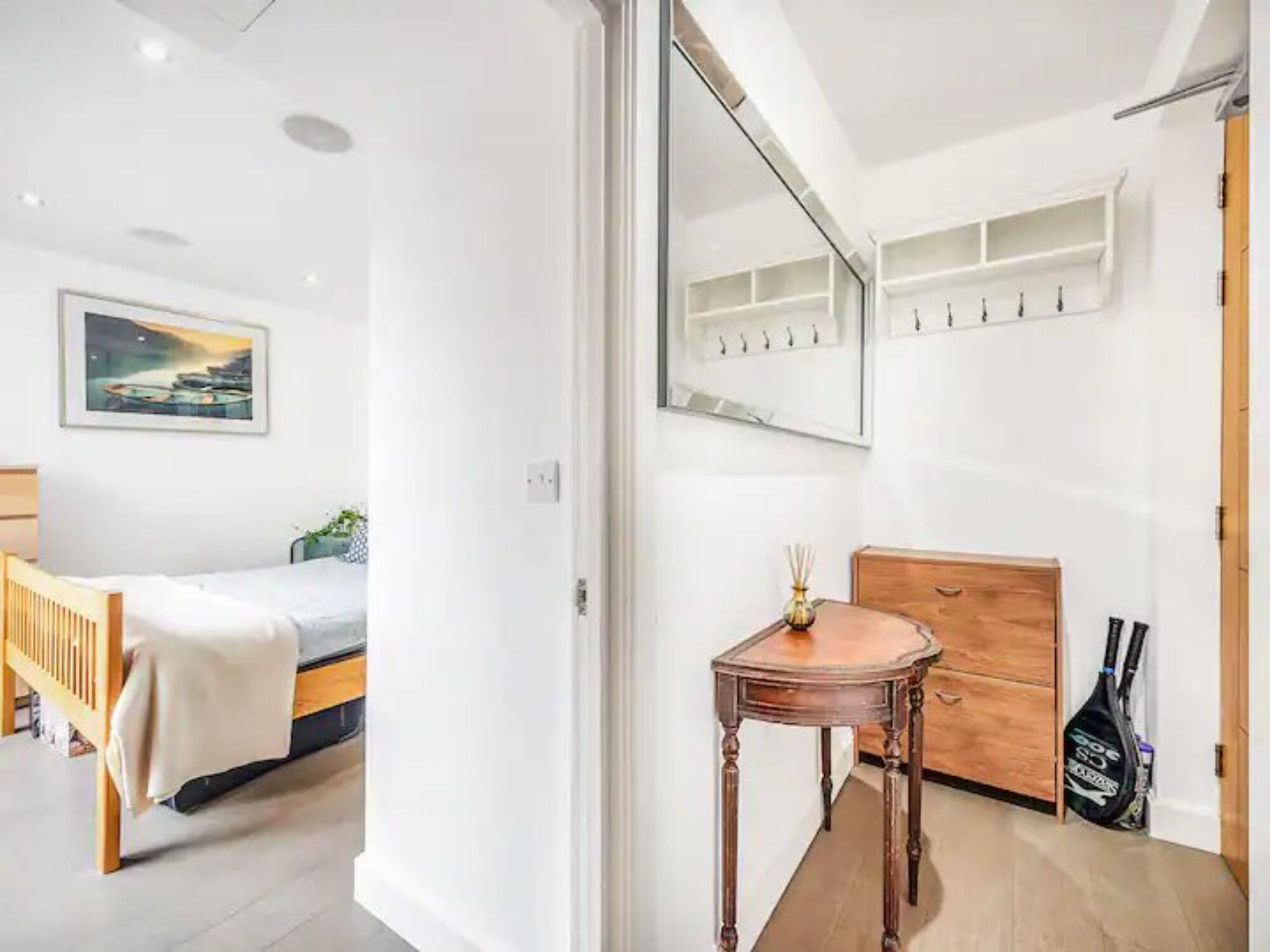 A modern bedroom with a bed, a wooden dresser, a small table with a vase, and a mirror on the wall.