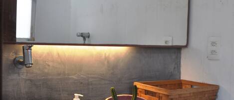 A bathroom with a white sink, a mirror, a wooden basket, and a decorative bowl with a cactus.