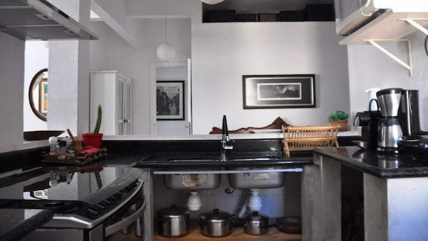 A compact kitchen with a stove, sink, and microwave. There are cabinets, a hanging light, and a framed picture on the wall. - COBERTURA DUPLEX COM TERRAÇO EM IPANEMA (Rio de Janeiro)