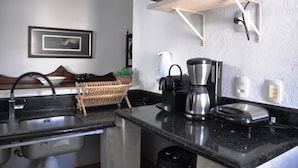 A kitchen with a black countertop, stainless steel appliances, a dish rack, and a wall-mounted shelf. - COBERTURA DUPLEX COM TERRAÇO EM IPANEMA (Rio de Janeiro)