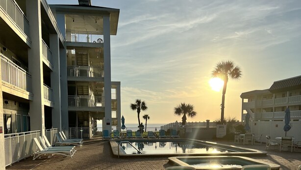 A pool area with lounge chairs and a view of the ocean at sunset. - Coastal Waters Cozy Studio unit 102 (New Smyrna Beach)