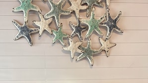 A room with a wall-mounted starfish decoration, a bedside table with a lamp, and two pillows. - Coastal Waters Cozy Studio unit 102 (New Smyrna Beach)
