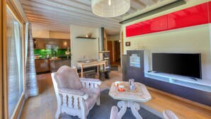 Una sala de estar moderna con televisor, una zona de comedor y una cocina al fondo.