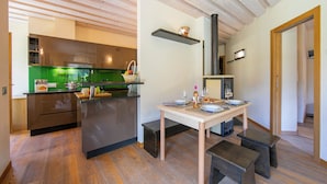 Una cocina moderna con techo de madera, un comedor con mesa lista para dos comensales y una pequeña zona de estar con bancos.