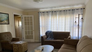 A living room with a brown sofa, a patterned ottoman, and a coffee table. There is a door with glass panels and a patterned curtain. - Beautiful Home in Ontonagon - 2 blocks from Lake Superior (Ontonagon)
