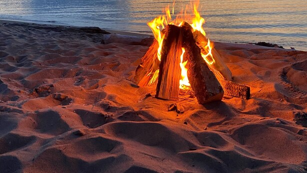 A campfire on a sandy beach with a view of the ocean and a sunset in the background. - Beautiful Home in Ontonagon - 2 blocks from Lake Superior (Ontonagon)