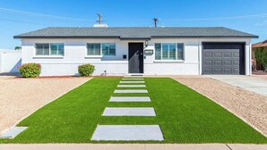 A single-story house with a dark front door, a garage, and a well-maintained lawn with stepping stones leading to the entrance. - Scottsdale Retreat | Pool, Putt & More (Scottsdale)