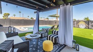 An outdoor patio with a pool, black and white striped sofas, a yellow ottoman, and a table with a remote control. - Scottsdale Retreat | Pool, Putt & More (Scottsdale)